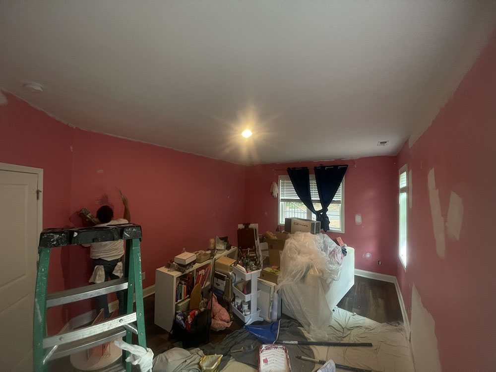 Painter cutting in wall edges and patching surface blemishes in bedroom